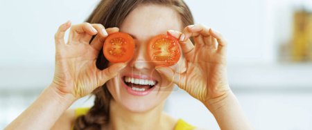 Photo for Happy young woman holding two slices of tomato in front of eyes - Royalty Free Image