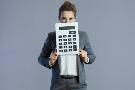 Téléchargez les photos : Élégante femme d'âge moyen ouvrière en costume gris avec calculatrice sur fond gris. - en image libre de droit
