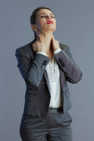 Photo for Tired elegant 40 years old business woman in gray suit having neck pain against gray background. - Royalty Free Image