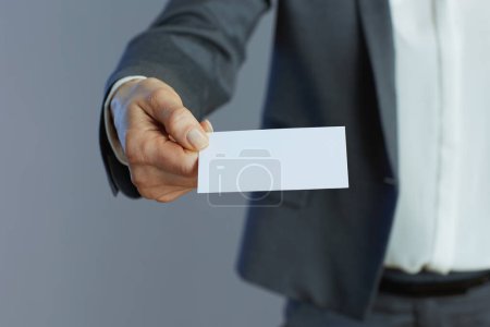 Photo for Closeup on middle aged woman employee in gray suit with business card isolated on gray. - Royalty Free Image