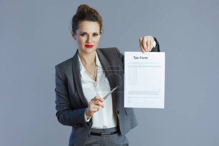 Photo for Modern small business owner woman in gray suit with tax form isolated on gray background. - Royalty Free Image