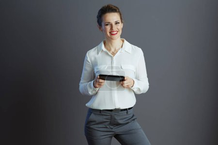 Téléchargez les photos : Heureuse femme élégante travailleur en chemisier blanc écriture sms à partir d'un smartphone sur fond gris. - en image libre de droit