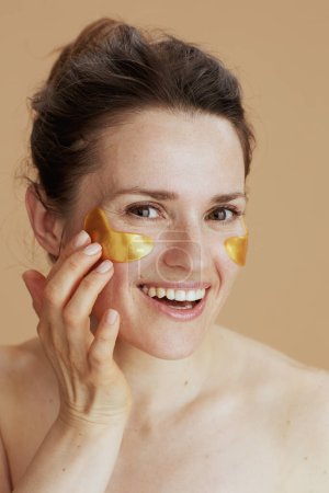 Téléchargez les photos : Heureuse jeune femme avec des patchs pour les yeux isolés sur beige. - en image libre de droit