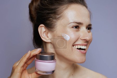 Téléchargez les photos : Femme moderne souriante avec pot de crème cosmétique isolé sur fond bleu. - en image libre de droit