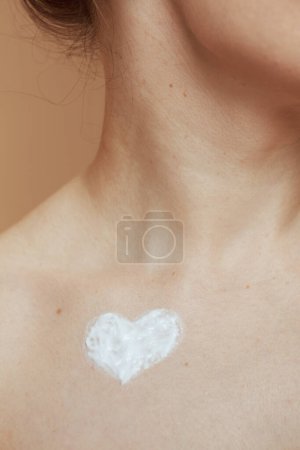 Téléchargez les photos : Gros plan sur femme moderne de 40 ans avec de la crème en forme de coeur sur la poitrine. - en image libre de droit