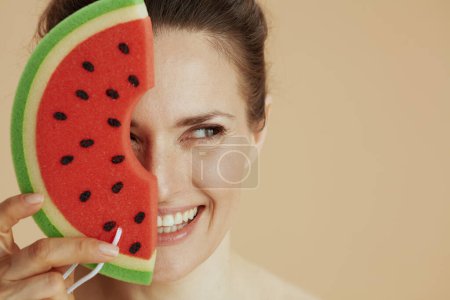 Téléchargez les photos : Femme moderne souriante avec éponge de douche pastèque isolée sur beige. - en image libre de droit