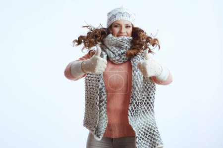 Foto de Hola invierno. mujer con estilo en suéter, mitones, sombrero y bufanda contra fondo blanco que muestra los pulgares hacia arriba y saltando. - Imagen libre de derechos