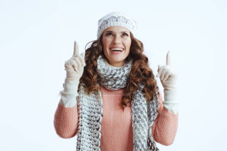 Photo for Hello winter. smiling stylish female in sweater, mittens, hat and scarf against white background pointing up on copy space. - Royalty Free Image