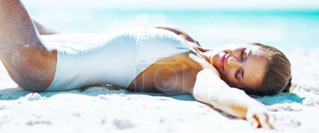 Foto de Mujer joven y relajada en traje de baño tomando el sol en la playa de arena - Imagen libre de derechos
