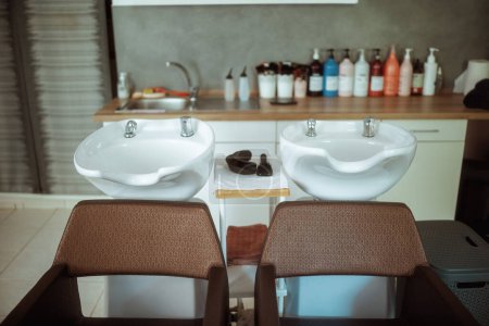 Foto de Moderno salón de belleza con sillas, botellas de productos para el cuidado del cabello y la unidad de lavado posterior del salón. - Imagen libre de derechos