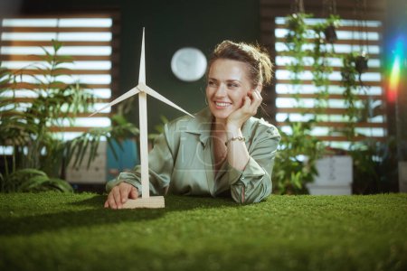 Photo for Sustainable business. smiling young small business owner woman in green blouse in modern green office with windmill - Royalty Free Image