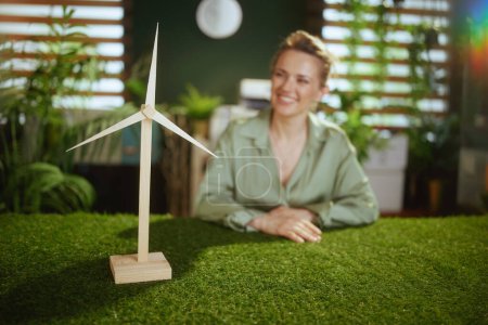 Foto de Eco Negocios. Primer plano de la mujer de negocios feliz en blusa verde en oficina verde con molino de viento - Imagen libre de derechos