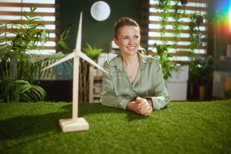 Téléchargez les photos : Eco Business. souriant moyen propriétaire de petite entreprise femme en chemisier vert dans le bureau vert moderne avec moulin à vent - en image libre de droit