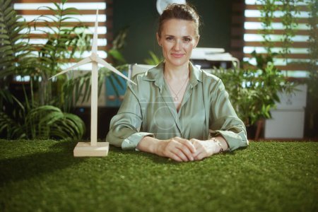 Foto de Mujer de negocios de mediana edad en blusa verde en moderna oficina verde con molino de viento - Imagen libre de derechos