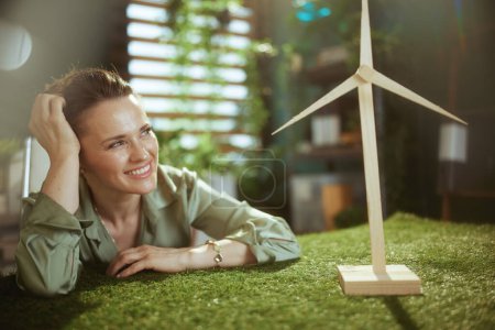Foto de Tendencias ecológicas. sonriente moderna propietaria de una pequeña empresa mujer en blusa verde en moderna oficina verde con molino de viento - Imagen libre de derechos