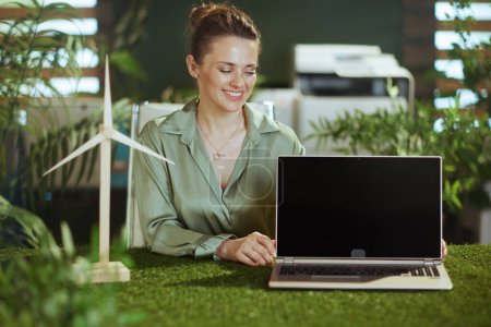 Photo for Happy modern middle aged small business owner woman in green blouse in modern green office with windmill showing laptop blank screen - Royalty Free Image