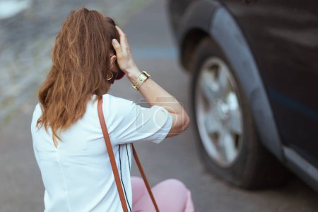 Foto de Accidente de coche. Primer plano de la mujer turística estresada en la ciudad cerca de coche con neumático pinchado. - Imagen libre de derechos