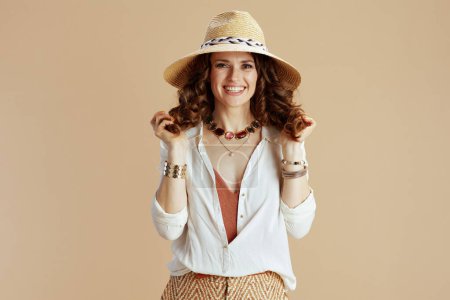 Téléchargez les photos : Vacances à la plage. femme moderne et souriante d'âge moyen en chemisier blanc et short sur fond beige avec chapeau de paille. - en image libre de droit
