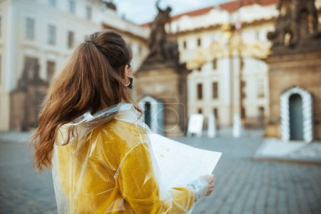 Foto de Visto desde atrás mujer turista en blusa amarilla y impermeable en Praga República Checa con mapa cerca del Castillo de Praga. - Imagen libre de derechos