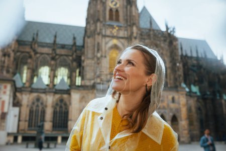 Photo for Smiling young tourist woman in yellow blouse and raincoat in Prague Czech Republic having walking tour. - Royalty Free Image