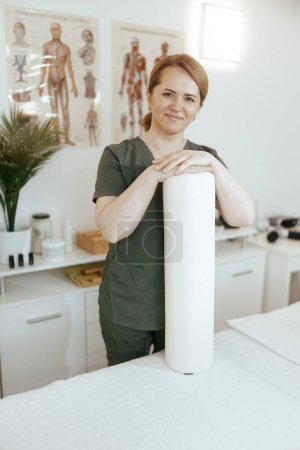 Photo for Healthcare time. happy female massage therapist in massage cabinet with disposable sheet preparing for new client. - Royalty Free Image