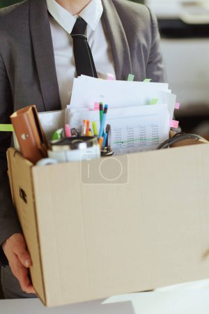 Photo for New job. Closeup on modern 40 years old woman worker in modern green office in grey business suit with personal belongings in cardboard box. - Royalty Free Image