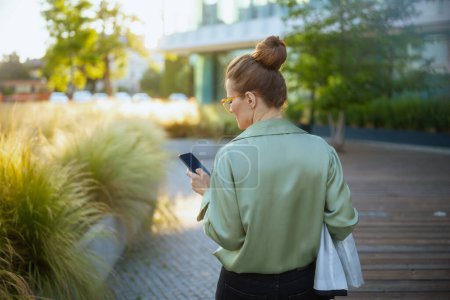 Téléchargez les photos : Vu de derrière travailleuse près du centre d'affaires en chemisier vert avec smartphone. - en image libre de droit