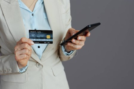 Foto de Primer plano de la trabajadora en un traje de trabajo ligero con smartphone y tarjeta de crédito aislada sobre fondo gris. - Imagen libre de derechos