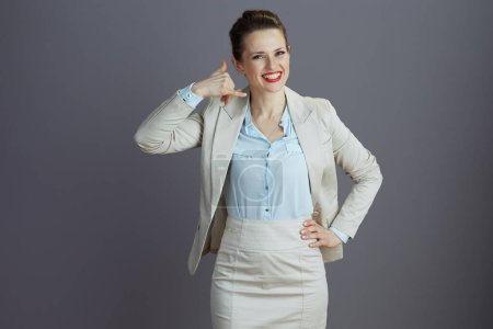 Foto de Sonriente de moda 40 años de edad, empleada en un traje de negocios ligero que muestra llámame gesto aislado sobre fondo gris. - Imagen libre de derechos