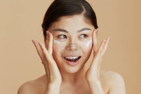 Téléchargez les photos : Moderne asiatique femelle avec visage crème sur fond beige. - en image libre de droit