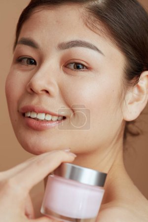 Foto de Retrato de mujer moderna con frasco de crema facial sobre fondo beige. - Imagen libre de derechos