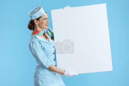 Photo for Smiling modern stewardess woman isolated on blue background in blue uniform showing blank board. - Royalty Free Image