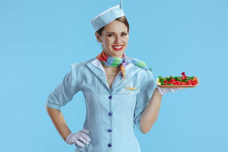 Photo for Smiling stylish female flight attendant against blue background in blue uniform with candies. - Royalty Free Image