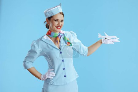 Foto de Mujer azafata con estilo sonriente sobre fondo azul en uniforme azul con un pequeño avión. - Imagen libre de derechos