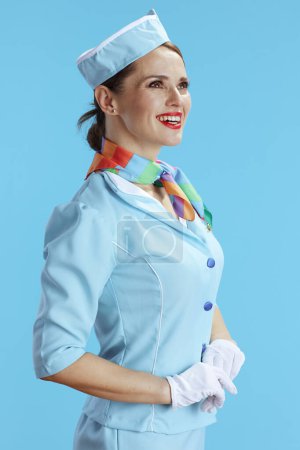 Téléchargez les photos : Femme hôtesse moderne souriante sur fond bleu en uniforme bleu regardant au loin. - en image libre de droit
