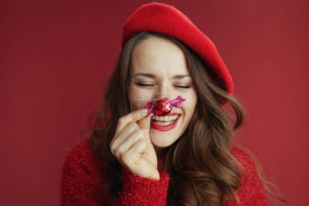 Téléchargez les photos : Joyeux Valentin. sourire élégant femme âgée de 40 ans en pull rouge et béret avec bonbons et longs cheveux ondulés. - en image libre de droit