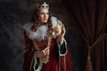 Téléchargez les photos : Reine médiévale en robe rouge avec masque vénitien, col blanc et couronne sur fond gris foncé. - en image libre de droit