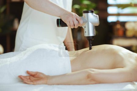 Photo for Healthcare time. Closeup on massage therapist in spa salon with massage pistol do a therapeutic massage on massage table. - Royalty Free Image