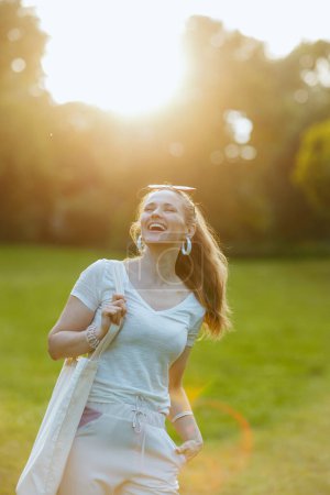 Foto de Hora de verano. feliz elegante mujer de 40 años de edad en camisa blanca con bolso de mano en el prado exterior en la naturaleza. - Imagen libre de derechos