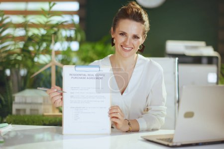 Photo for Eco real estate business. happy elegant female realtor in modern green office in white blouse with laptop, clipboard and document. - Royalty Free Image