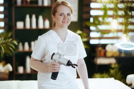 Photo for Healthcare time. happy female massage therapist in spa salon with massage pistol. - Royalty Free Image