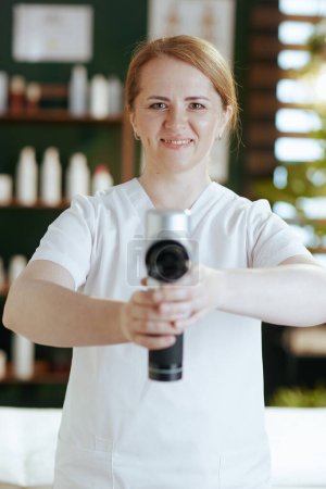 Photo for Healthcare time. happy massage therapist woman in massage cabinet with massage pistol. - Royalty Free Image