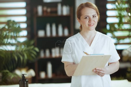 Foto de Tiempo de atención médica. terapeuta de masaje médico mujer feliz en el salón de spa con portapapeles. - Imagen libre de derechos