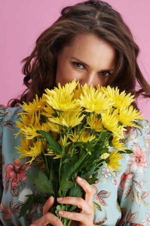 Photo for Smiling young woman in floral dress with yellow chrysanthemums flowers isolated on pink background. - Royalty Free Image
