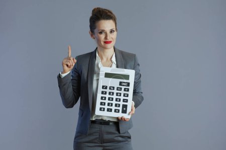 Téléchargez les photos : Femme d'affaires moderne de 40 ans en costume gris avec calculatrice isolée sur gris. - en image libre de droit