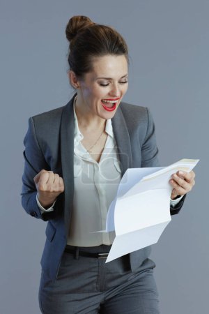 Foto de Feliz mujer de negocios de moda de 40 años en traje gris con documento aislado sobre fondo gris. - Imagen libre de derechos