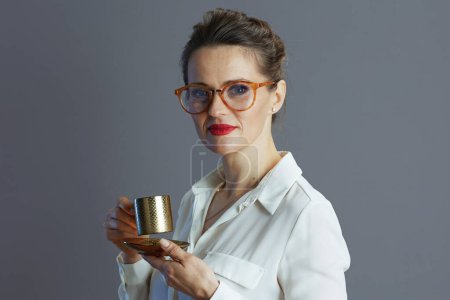 Téléchargez les photos : Femme d'âge moyen travailleur en chemisier blanc avec des lunettes et tasse de café isolé sur fond gris. - en image libre de droit