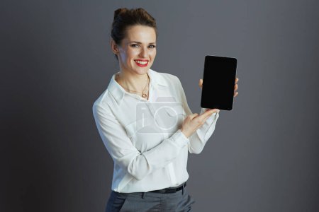 Foto de Sonriente joven propietaria de una pequeña empresa mujer en blusa blanca que muestra la pantalla en blanco de la tableta PC aislada sobre fondo gris. - Imagen libre de derechos