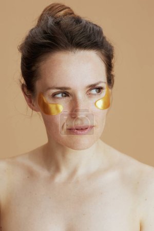 Téléchargez les photos : Chère jeune femme avec des patchs pour les yeux sur fond beige. - en image libre de droit