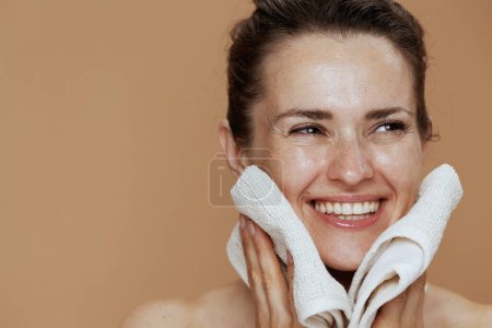 Téléchargez les photos : Heureuse femme moderne avec serviette lavage visage sur fond beige. - en image libre de droit